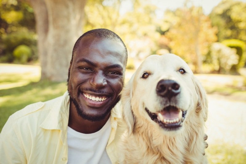 Smiling dog owner with a happy, healthy dog outdoors showing the results of good dog care